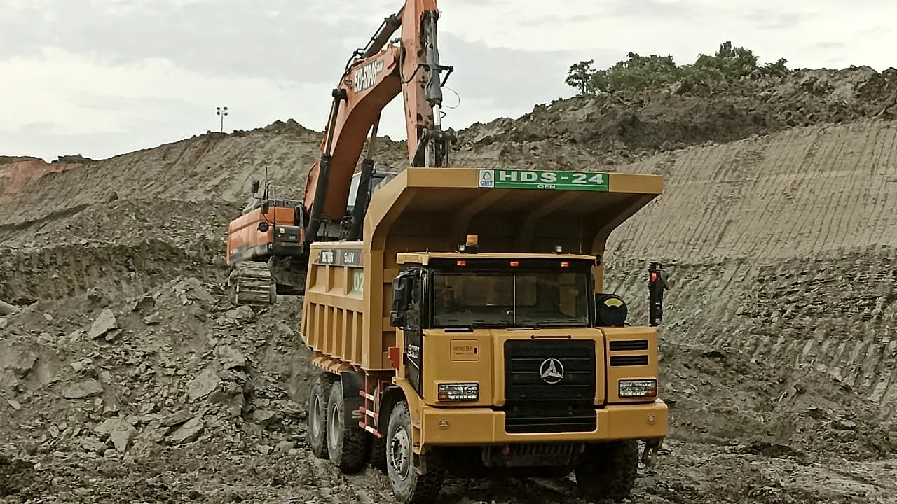 Haul truck and excavator working a bench under heavy cloud at an Indonesian coal mine.